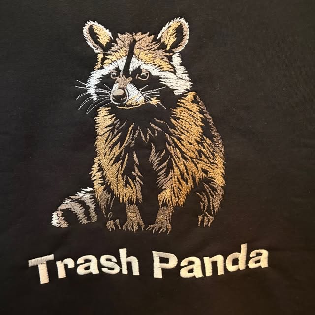 Photoreal raccoon embroidered in metallic-toned thread above the words Trash Panda on a black t-shirt by Raging Thunder Apparel